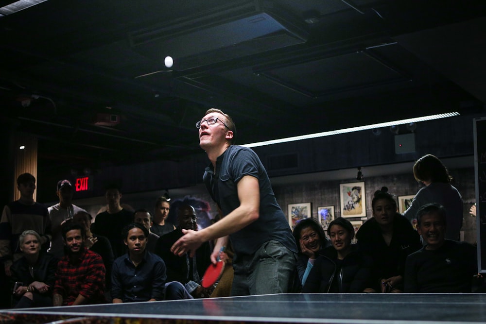 hombre a punto de remar pelota de ping pong rodeado de un grupo de personas