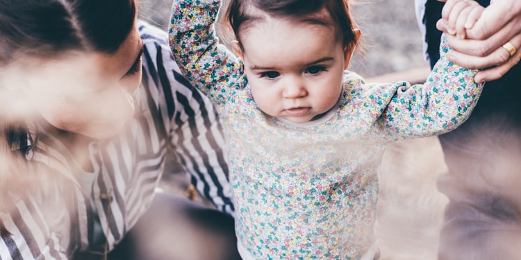 woman holding girl while learning to walk taken at daytime