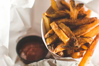 A close-up of crispy golden fries with a side of tangy dipping sauce on a maroon napkin.