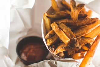 Golden crispy french fries served in a red container with ketchup on the side.