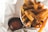 A close-up of crispy, golden-brown French fries served in a paper container, accompanied by a small black cup of ketchup set on a white napkin.