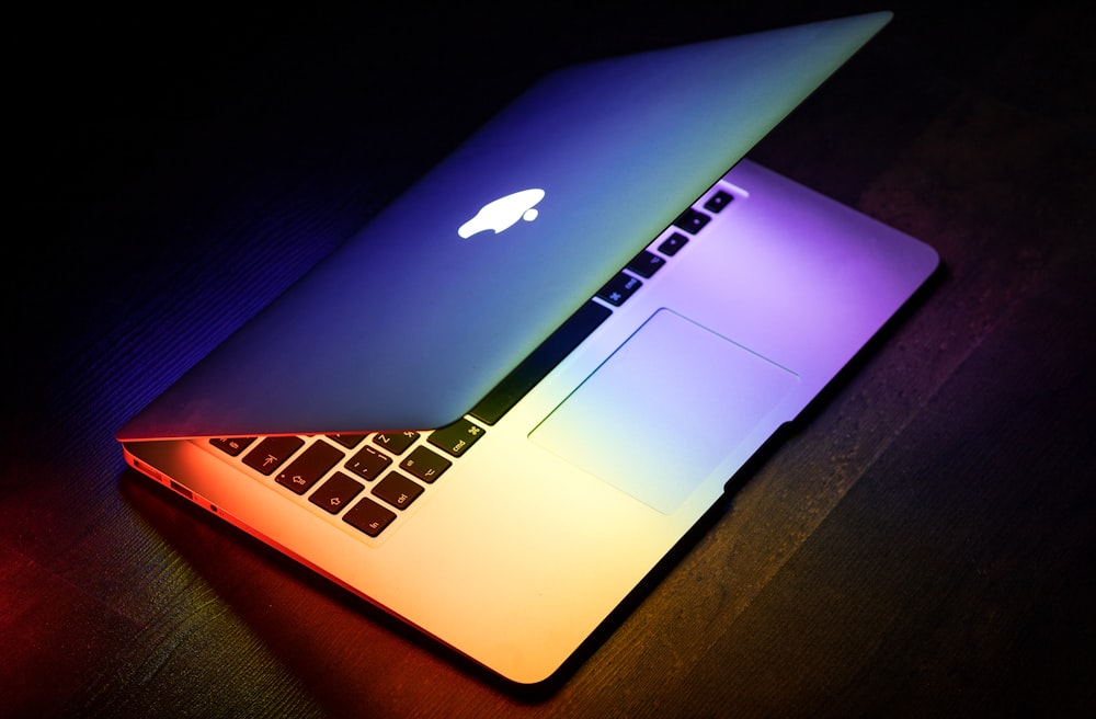 A MacBook lit up in rainbow colors on a wooden surface