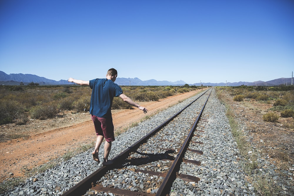 Persona che cammina sulla rotaia del treno in acciaio marrone all'aperto durante il giorno