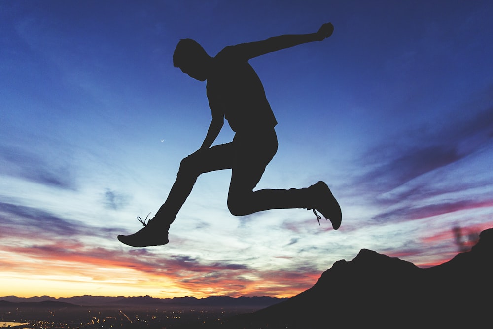 silhouette of man jumping near mountain