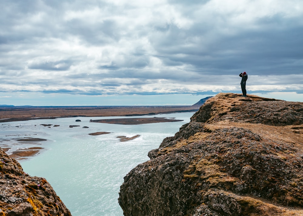 Person, die tagsüber auf einer Felsformation in der Nähe eines Gewässers steht
