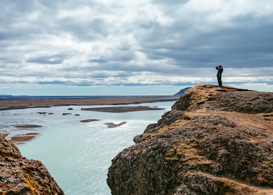 person standing on rock formation near body of water during daytime in Southern Region Iceland