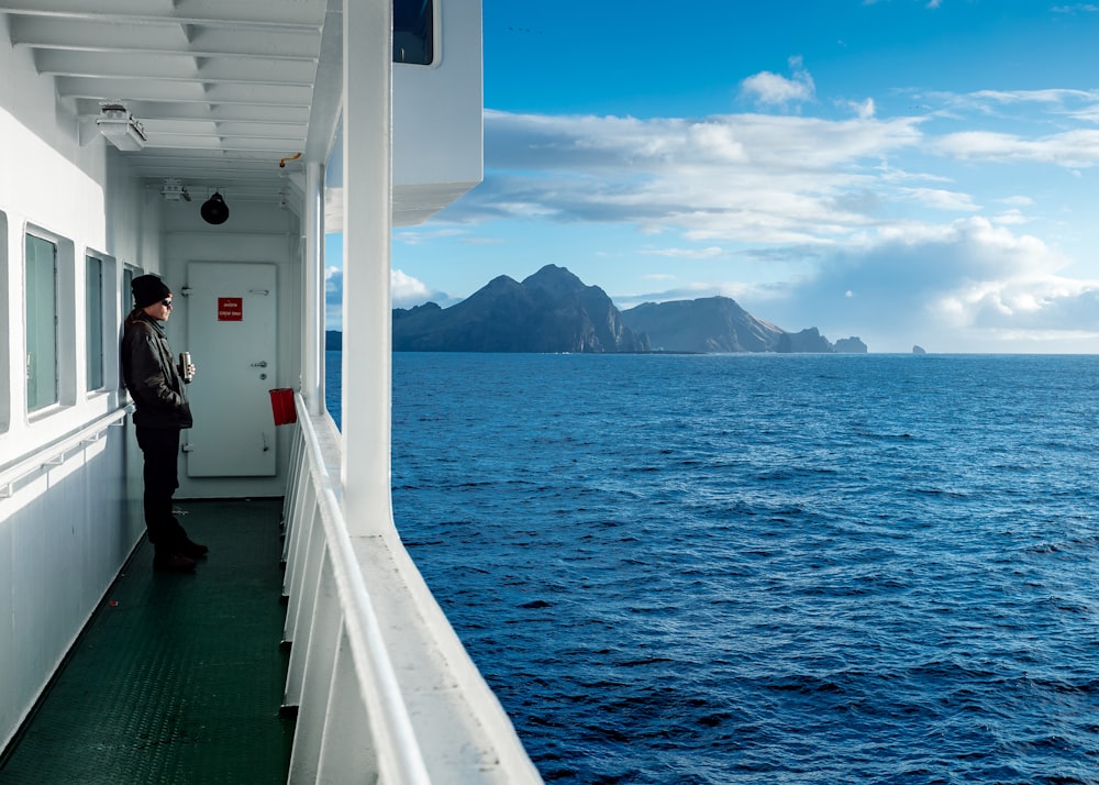 Humain en haut gris à manches longues portant une casquette en tricot noir s’appuyant sur la fenêtre du bateau tout en regardant l’eau de l’océan pendant la journée
