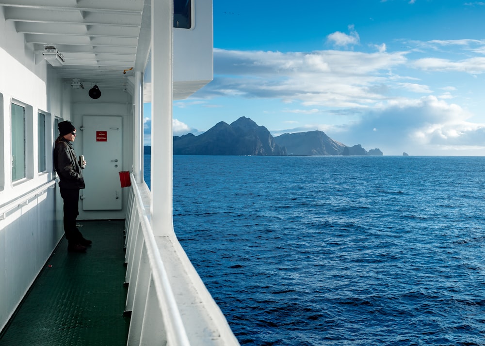 human in gray long-sleeved top wearing black knit cap leaning on boat window while looking on ocean water during daytime