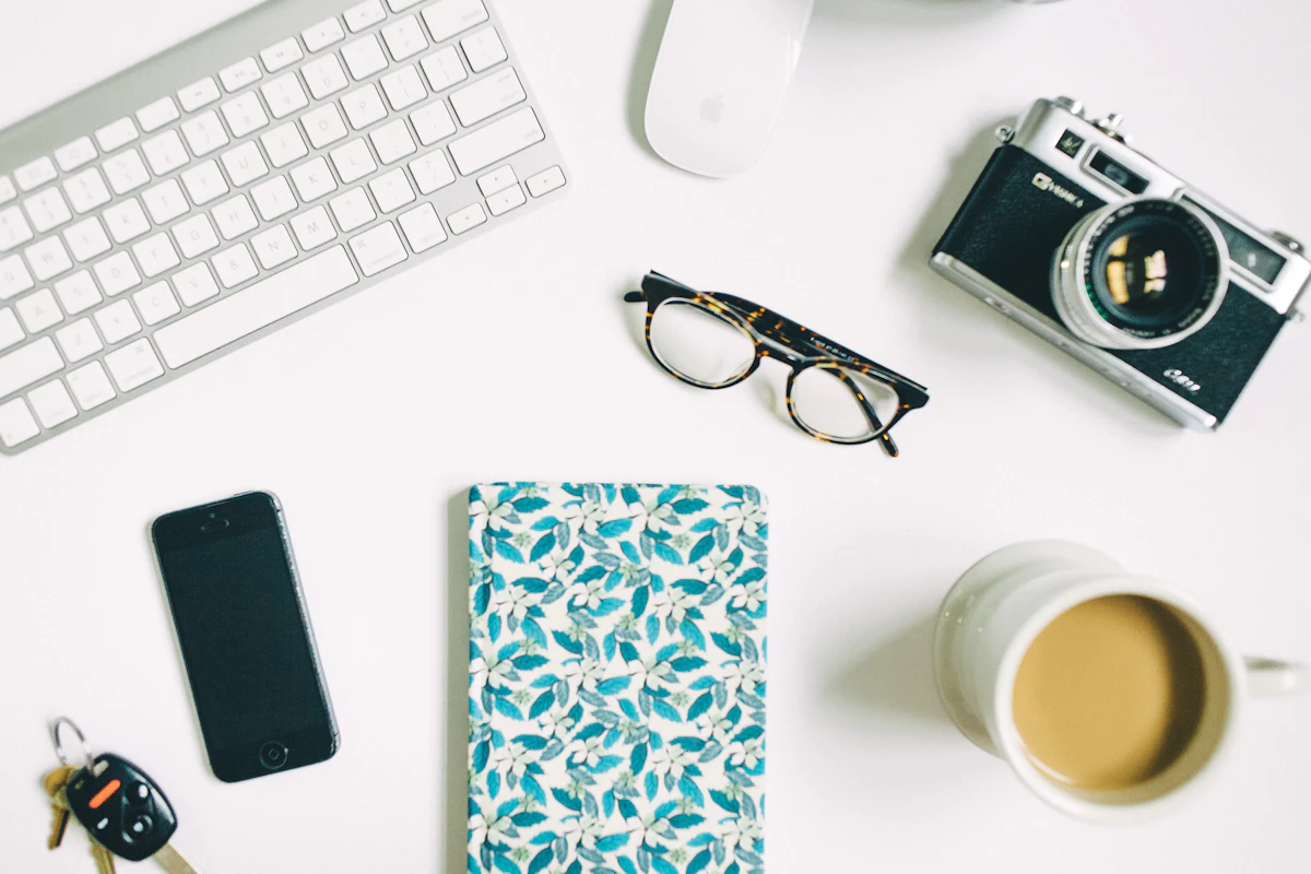 Flat lay of a camera, phone, glasses, notebook and coffee on a white desk