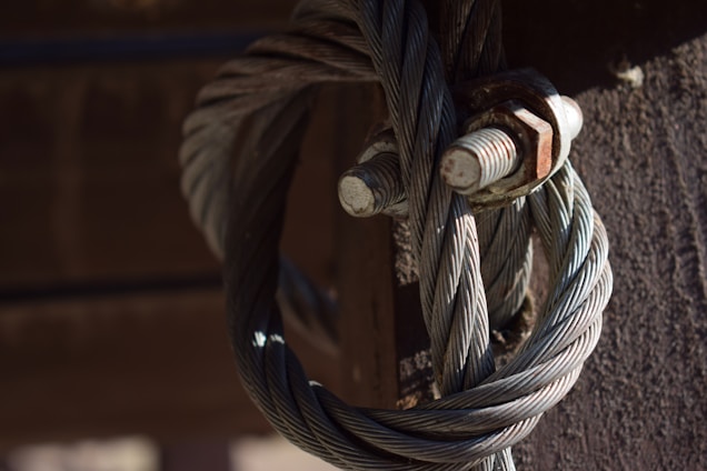 Thick intertwined steel cables are fastened together with large, rusted metal bolts against a dark background.