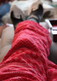 A person is lying down with their feet up, wearing fuzzy red patterned pants and thick socks. The focus is on the legs and feet, giving a cozy and relaxed atmosphere.