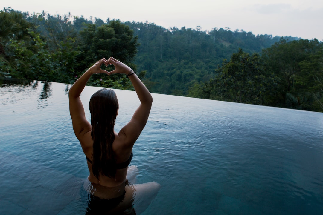 woman meditating in infinity pool making heart hand gesture 