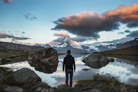 man standing on rocky cliff facing body of water