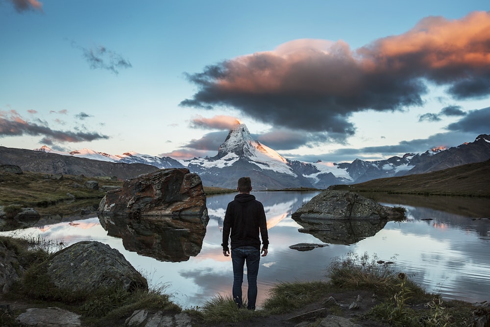 man standing on rocky cliff facing body of water