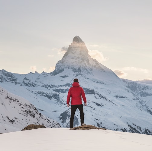 person in red hoodie standing on snowy mountain during daytime