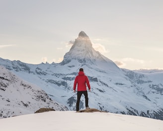 person in red hoodie standing on snowy mountain during daytime
