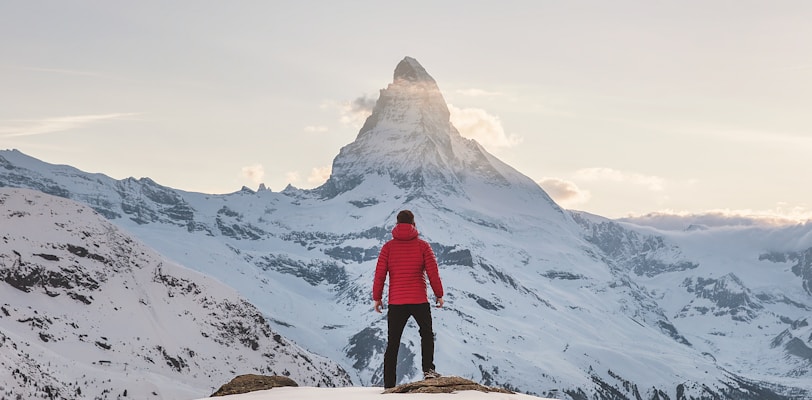 person in red hoodie standing on snowy mountain during daytime