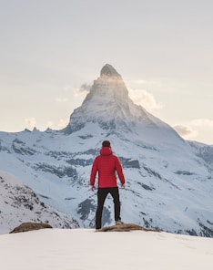 person in red hoodie standing on snowy mountain during daytime