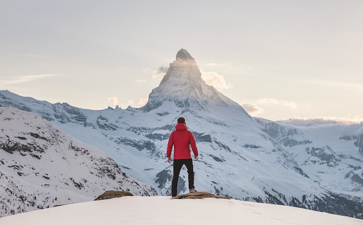 person in red hoodie standing on snowy mountain during daytime