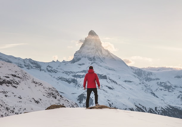 person in red hoodie standing on snowy mountain during daytime