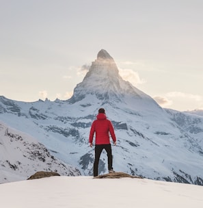 person in red hoodie standing on snowy mountain during daytime