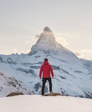 person in red hoodie standing on snowy mountain during daytime