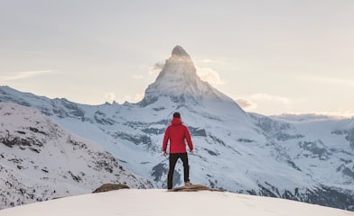 person in red hoodie standing on snowy mountain during daytime