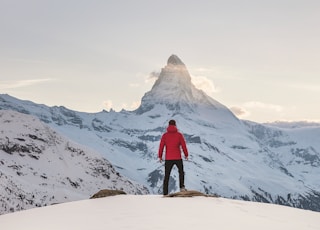 person in red hoodie standing on snowy mountain during daytime