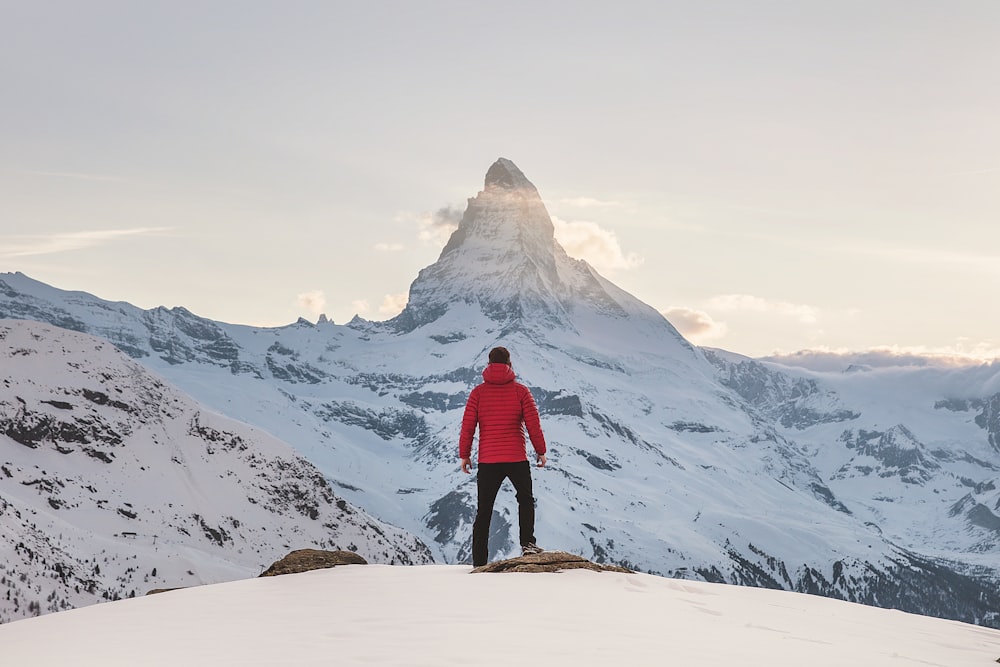 Persona in felpa con cappuccio rossa in piedi sulla montagna innevata durante il giorno