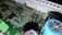 A close-up of a printed circuit board featuring various electronic components including integrated circuits, capacitors, and resistors. The green board is densely packed with intricate patterns and metallic connections. Some components have small markings, indicating their specifications.