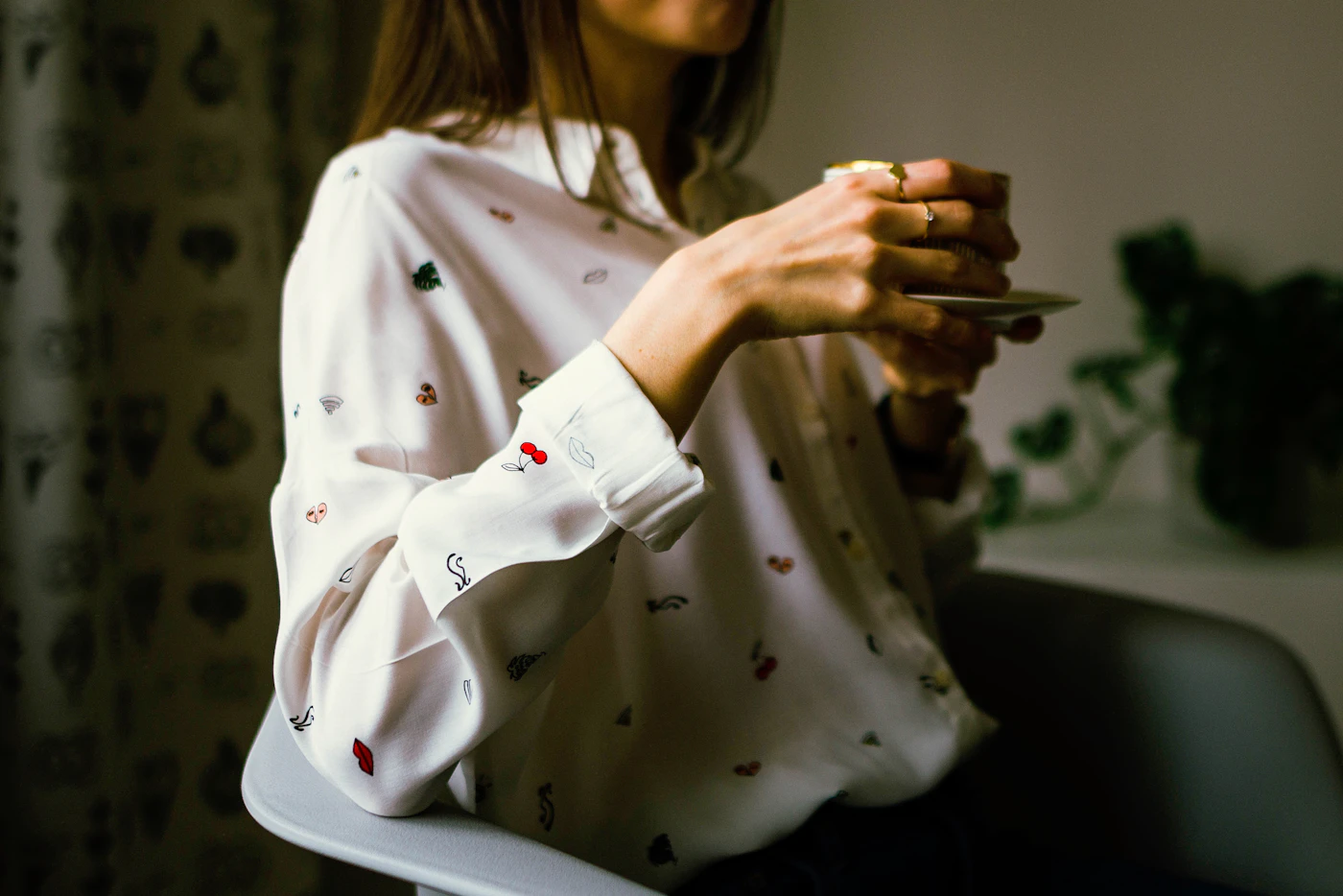 Woman in a white collared long-sleeve shirt holding a teacup in a sunlit room