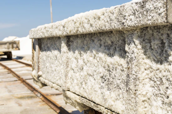 A close-up view of a salt-encrusted cart that appears to be on tracks, used for transporting salt. The cart is heavily coated with white salt crystals, suggesting an industrial or natural salt harvesting area.