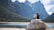 a couple sits on a rock looking out over a lake