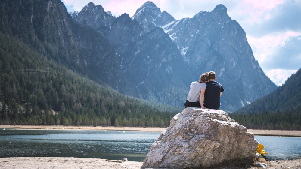 a couple sits on a rock looking out over a lake