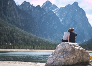 a couple sits on a rock looking out over a lake