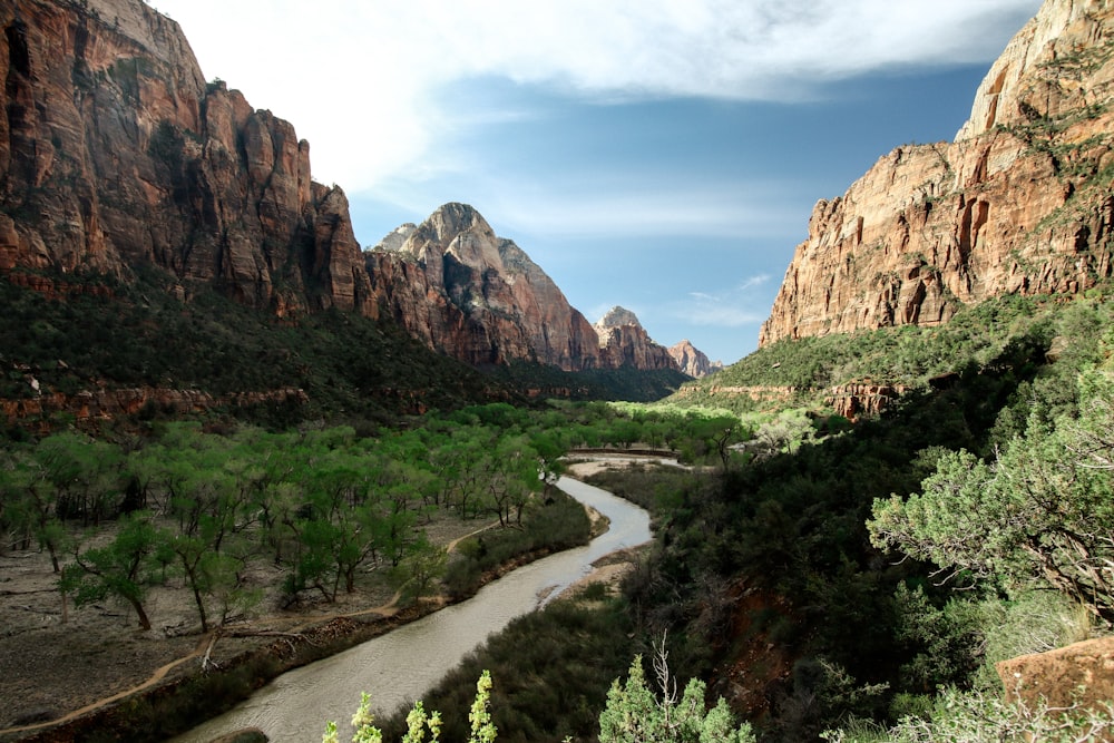 río que fluye cerca de árboles altos que ven la montaña bajo cielos azules y blancos