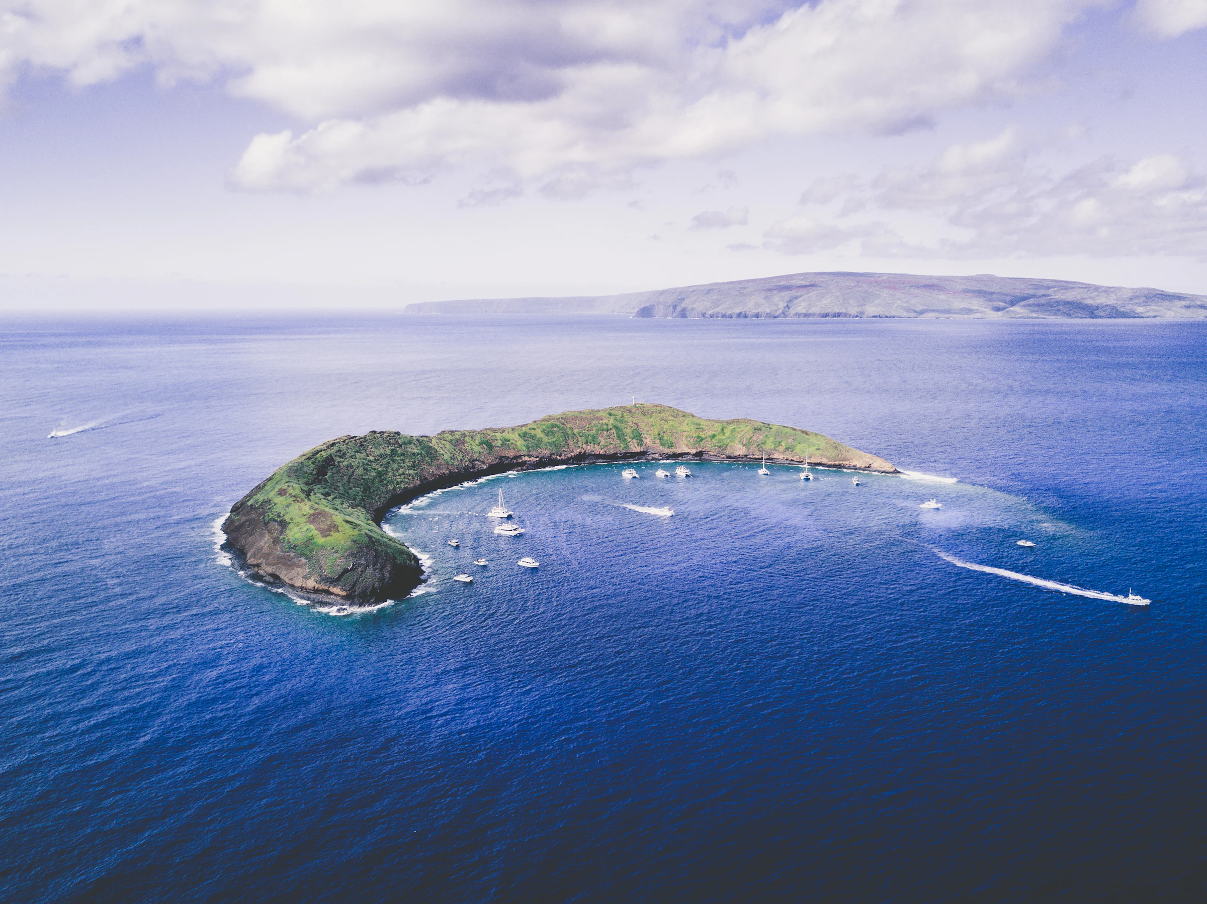 Aerial view of crescent-shaped Molokini with boats inside the cove