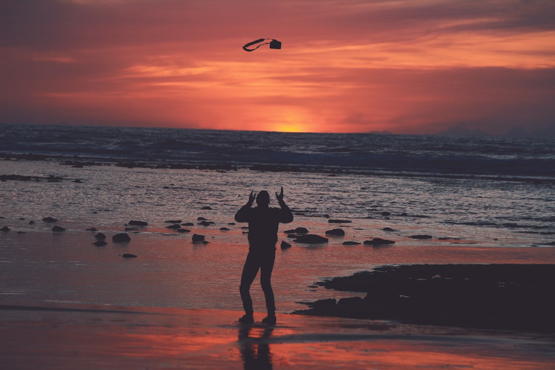 silhouette of woman standing on beach shore during sunset