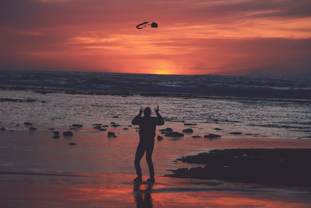 silhueta da mulher que está na praia da praia durante o pôr do sol