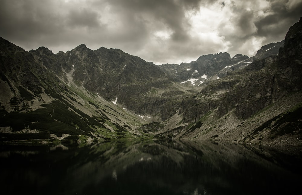 body of water overlooking mountains under white and gray cloudy skies at daytime