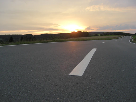 A freshly paved highway stretching through a green landscape at sunset.