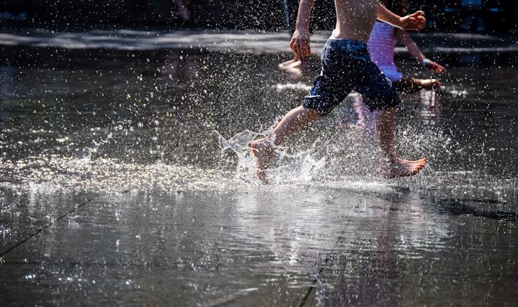 Happy children enjoying a summer camp activity, running through a sprinkler on a sunny day.