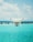 A drone is hovering in the foreground against a backdrop of a clear blue sky and a bright turquoise ocean. The design of the drone is sleek and modern, featuring a camera on its underside. The water and sky create a serene and expansive atmosphere.