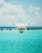 A drone is hovering in the foreground against a backdrop of a clear blue sky and a bright turquoise ocean. The design of the drone is sleek and modern, featuring a camera on its underside. The water and sky create a serene and expansive atmosphere.