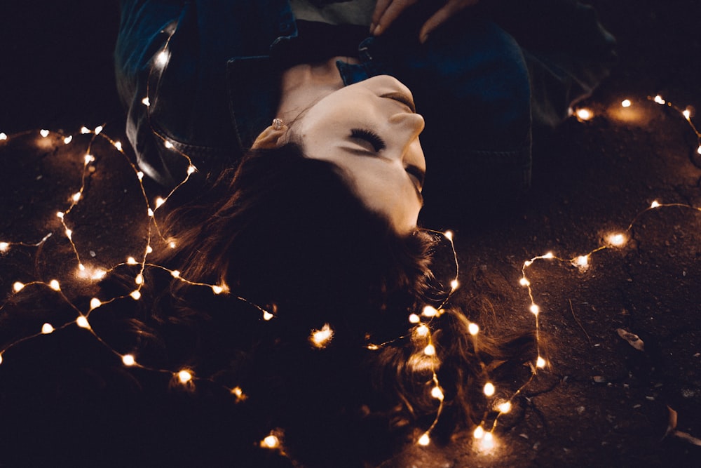 woman lying on yellow string lights
