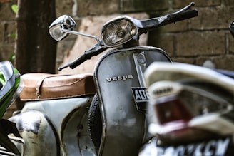A vintage Spanish Vespa scooter parked beside a rustic workshop with tools hanging on the wall.