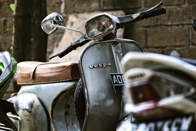 A vintage Spanish Vespa scooter parked beside a rustic workshop with tools hanging on the wall.