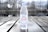A clear plastic bottle of Evian natural mineral water standing upright on a wooden surface. The bottle is 500 ml in size and has water droplets on it. In the background, there is a blurred, wintry outdoor setting with bare trees and a body of water, adding a sense of cold and serenity to the image.