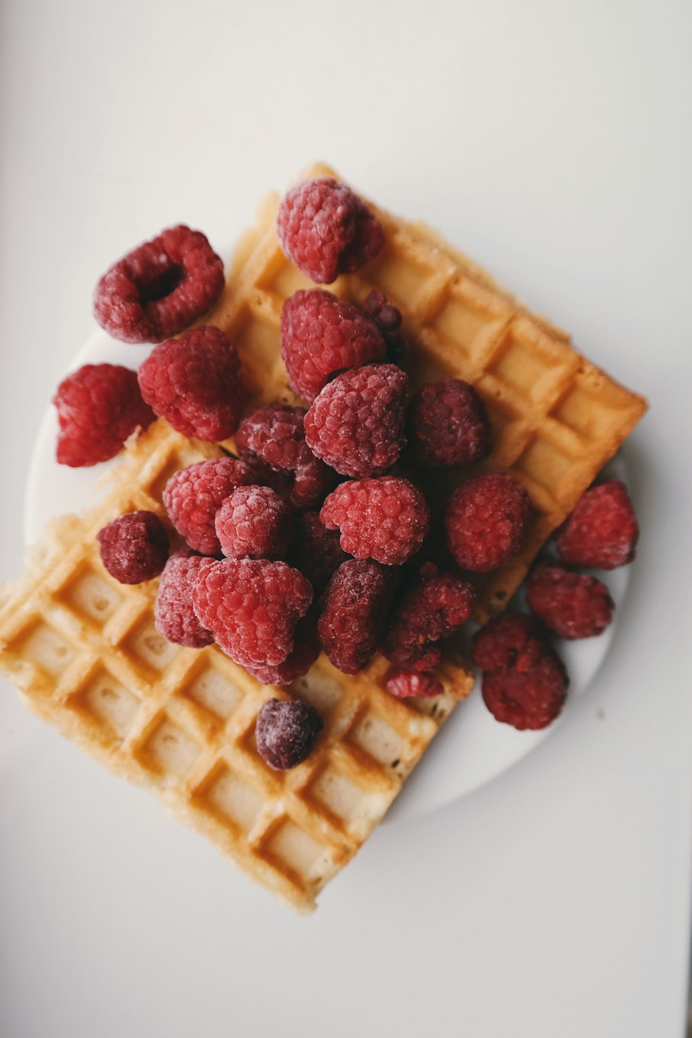 Raspberries on top of a rectangle shaped waffle.
