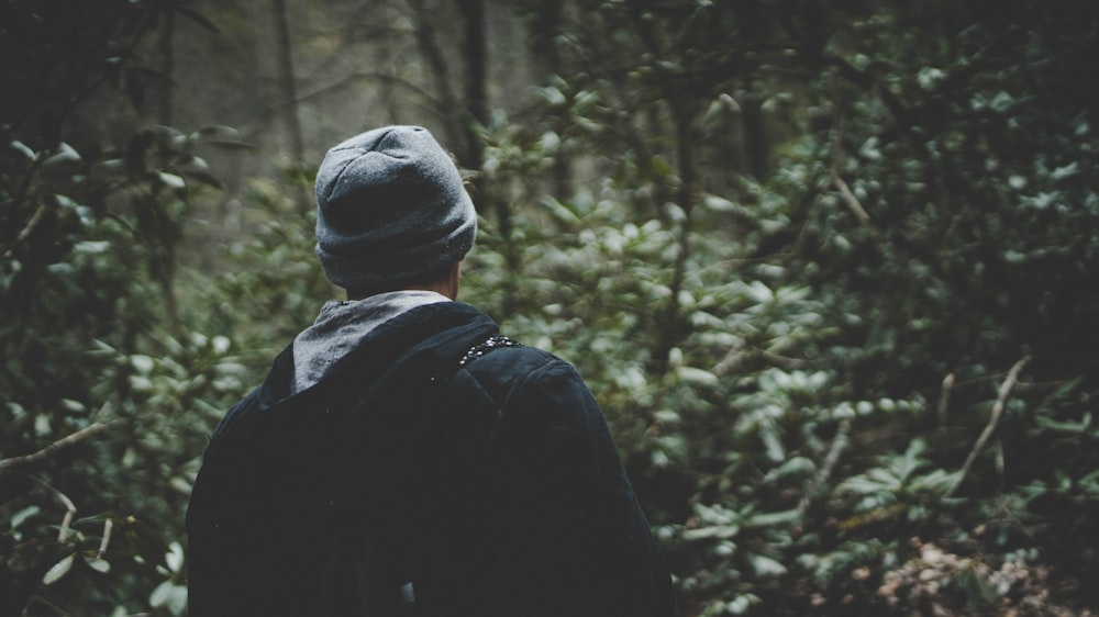 personne en sweat à capuche noir et portant un bonnet gris dans la forêt